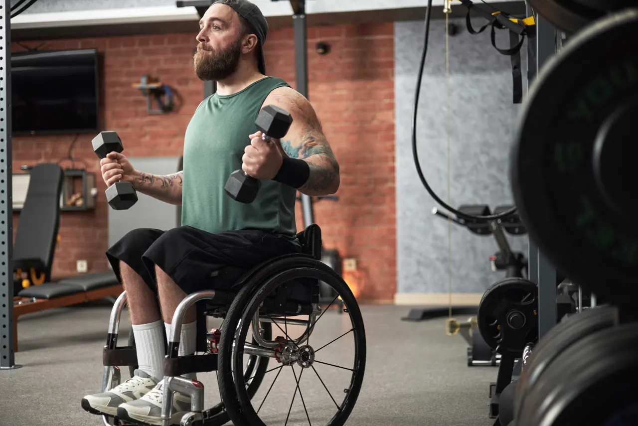 An athlete in a wheelchair lifts dumbbells during a workout.