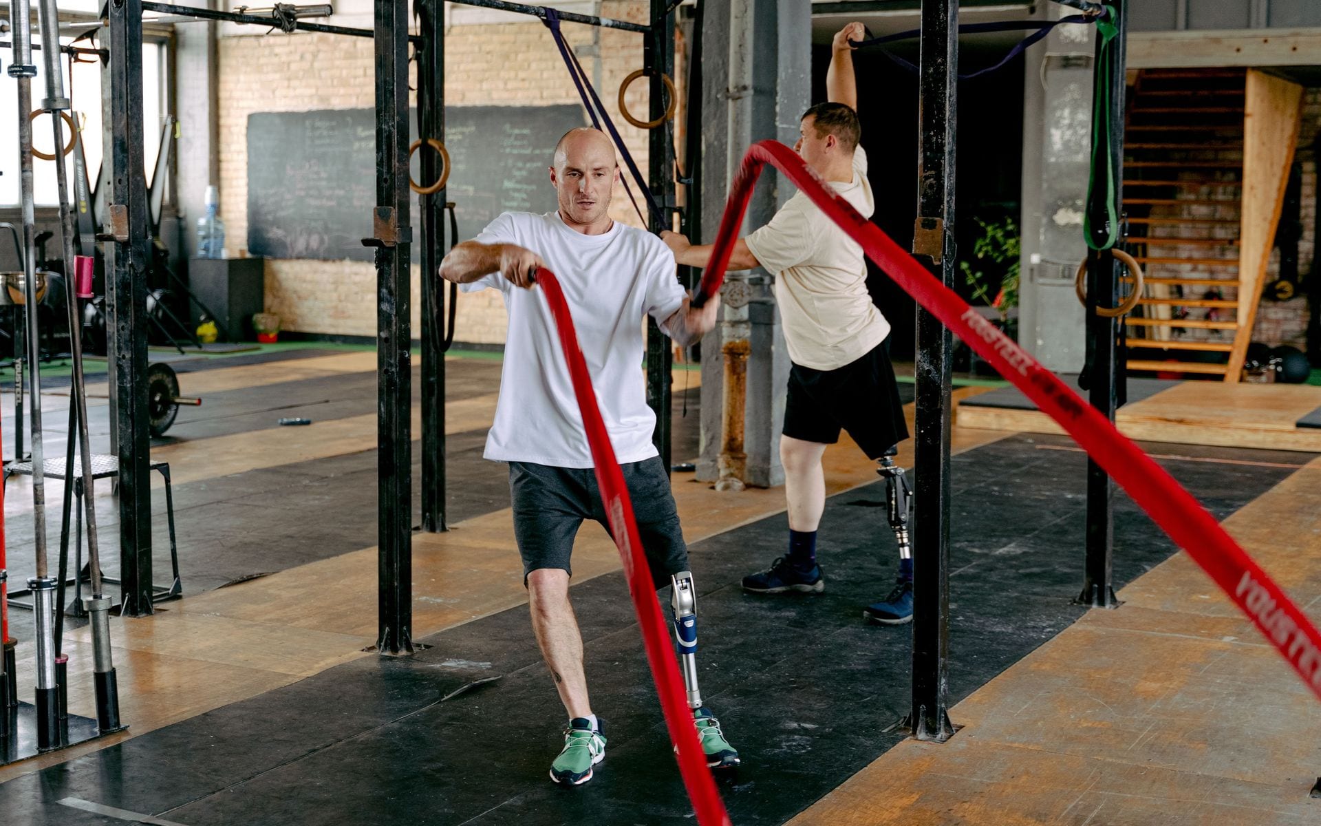 An athlete with a prosthetic leg using battle ropes while another athlete exercises behind him.