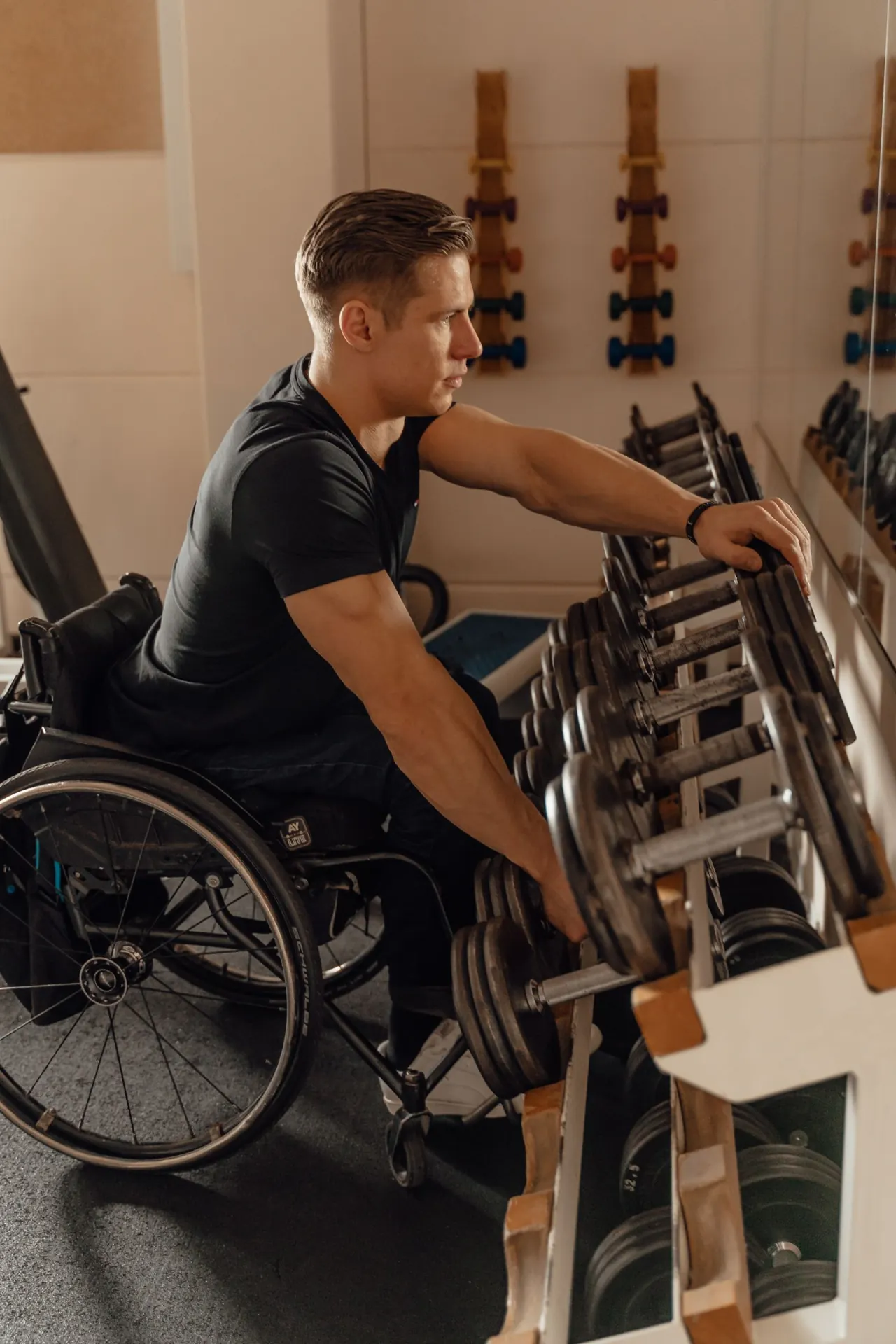 A man in a wheelchair reaches for a dumbbell on a rack.