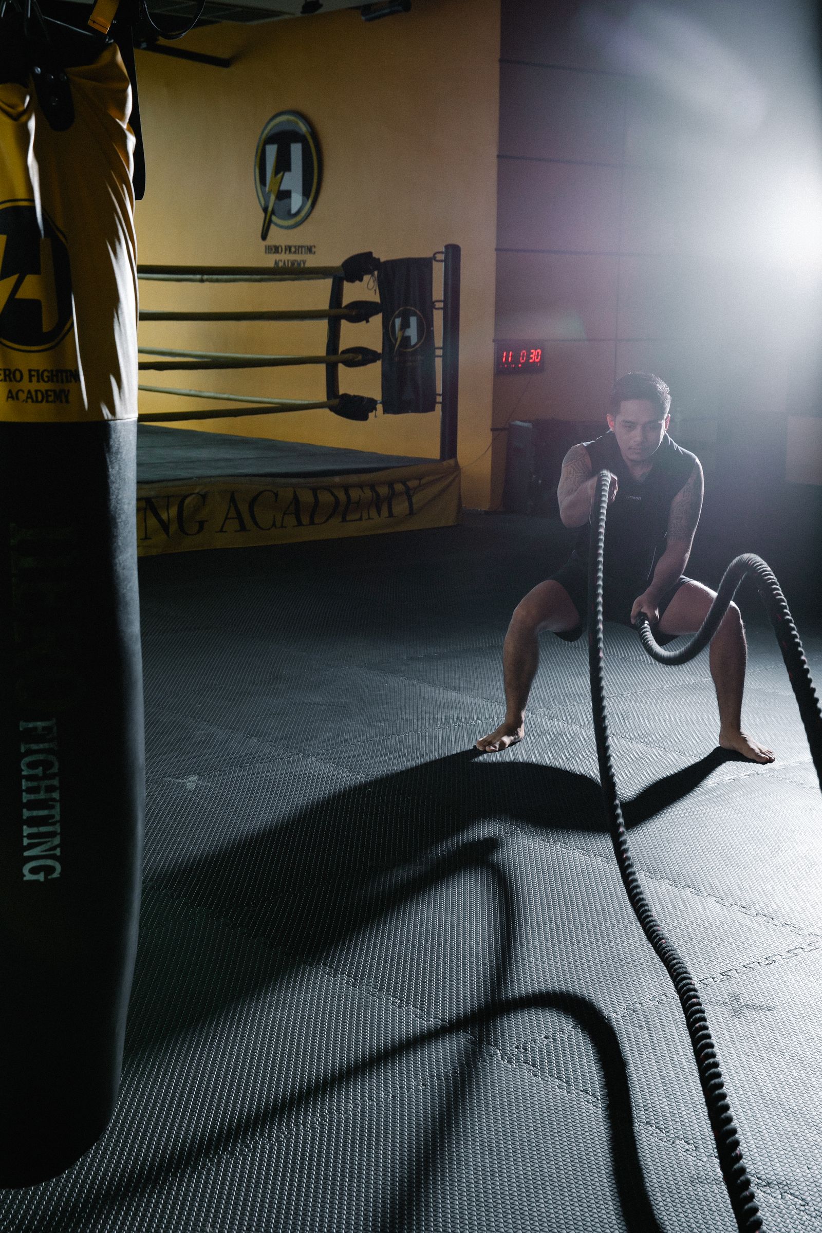 An athlete swings battle ropes in a dimly lit boxing gym.