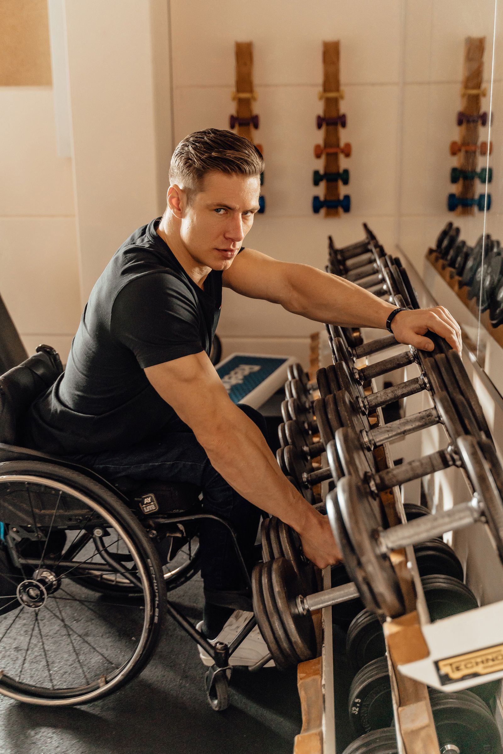 A man in a wheelchair selects a dumbbell from a rack.